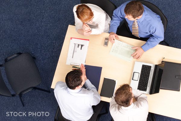Attorneys, client, & court reporter sitting at a conference table during a deposition.